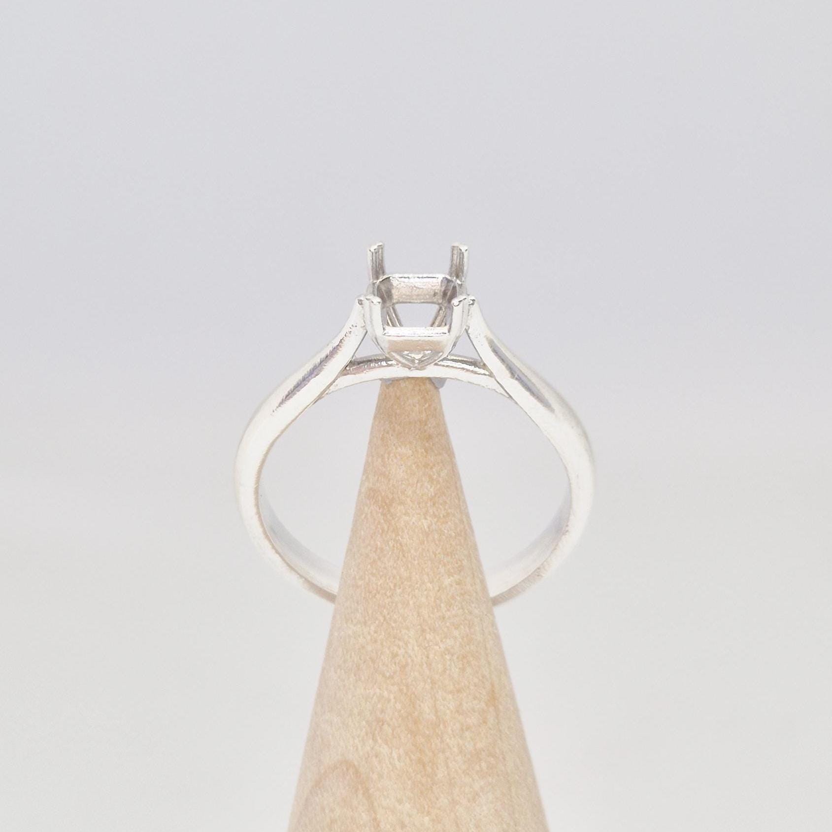 Front-facing view of a sterling silver ring setting with a four-prong princess cut head, displayed on a conical wooden stand, with the band arching elegantly towards the setting.