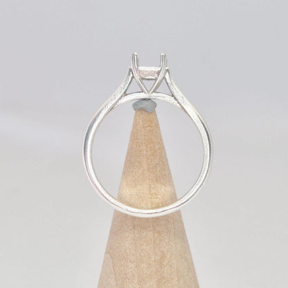 Back view of a sterling silver ring setting with a four-prong princess cut head, displayed on a conical wooden stand, showing the complete circular band and the base of the setting.