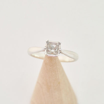 Frontal view of a sterling silver ring setting with a four-prong princess cut head, centered on a conical wooden stand, showcasing the distinct square shape of the prongs.