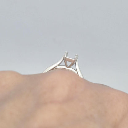 Close-up of a sterling silver ring setting with a four-prong princess cut head, seen from a low angle on a finger, emphasizing the open basket design under the stone setting.