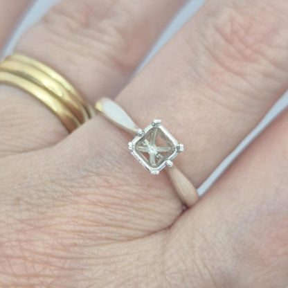 Sterling silver ring setting with a four-prong princess cut head, worn on a hand, showing a simple gold band on the same finger. The setting's open basket is visible from a top-down angle.