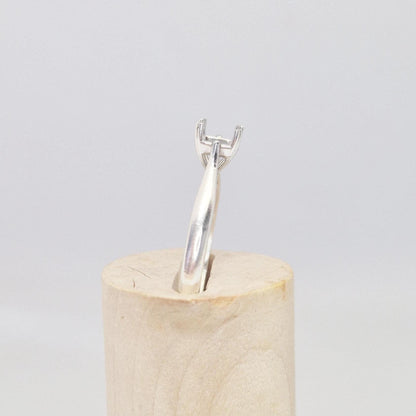 Profile view of a sterling silver ring setting with a four-prong princess cut head, standing upright in a cylindrical wooden stand, highlighting the elevated setting.