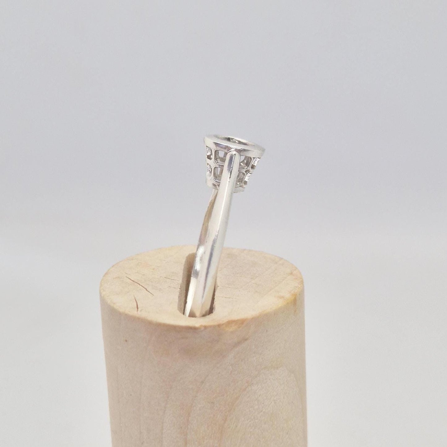 Side view of a silver ring setting with an empty round bezel, displayed upright on a light wooden cone. The ring band is smooth and tapers slightly towards the setting.