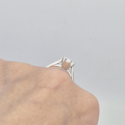 Close-up of a sterling silver ring setting with a cushion cut bezel, worn on a hand, showing the smooth, polished surface of the bezel from a low angle.