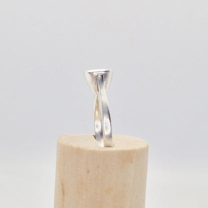 Profile view of a sterling silver ring setting with a cushion cut bezel, standing upright in a cylindrical wooden stand, highlighting the smooth band and the flush bezel.
