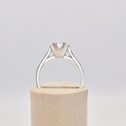 Frontal close-up of a sterling silver ring setting with a cushion cut bezel, presented on a cylindrical wooden stand, focusing on the details of the bezel setting.