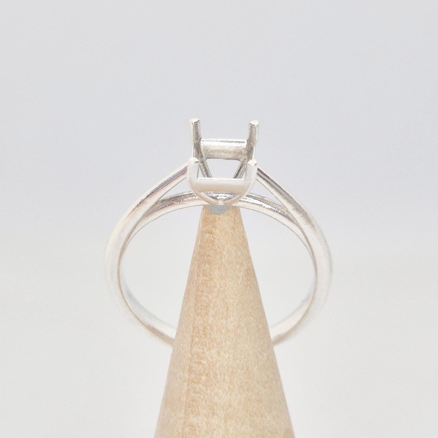 Silver cathedral setting princess cut ring blank on a conical wooden ring holder, viewed from the front, showing the empty four-prong setting and the band.