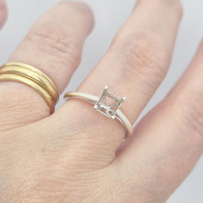 Silver cathedral setting princess cut ring blank on a hand, next to a plain gold band, showcasing how the ring sits on a finger and the empty four-prong setting.