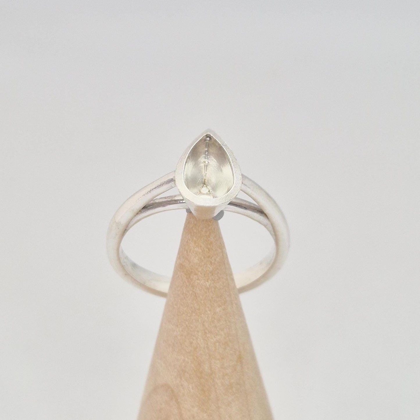 Silver pear cut bezel cathedral ring blank on a conical wooden ring holder, front view, showing the empty pear-shaped bezel setting.