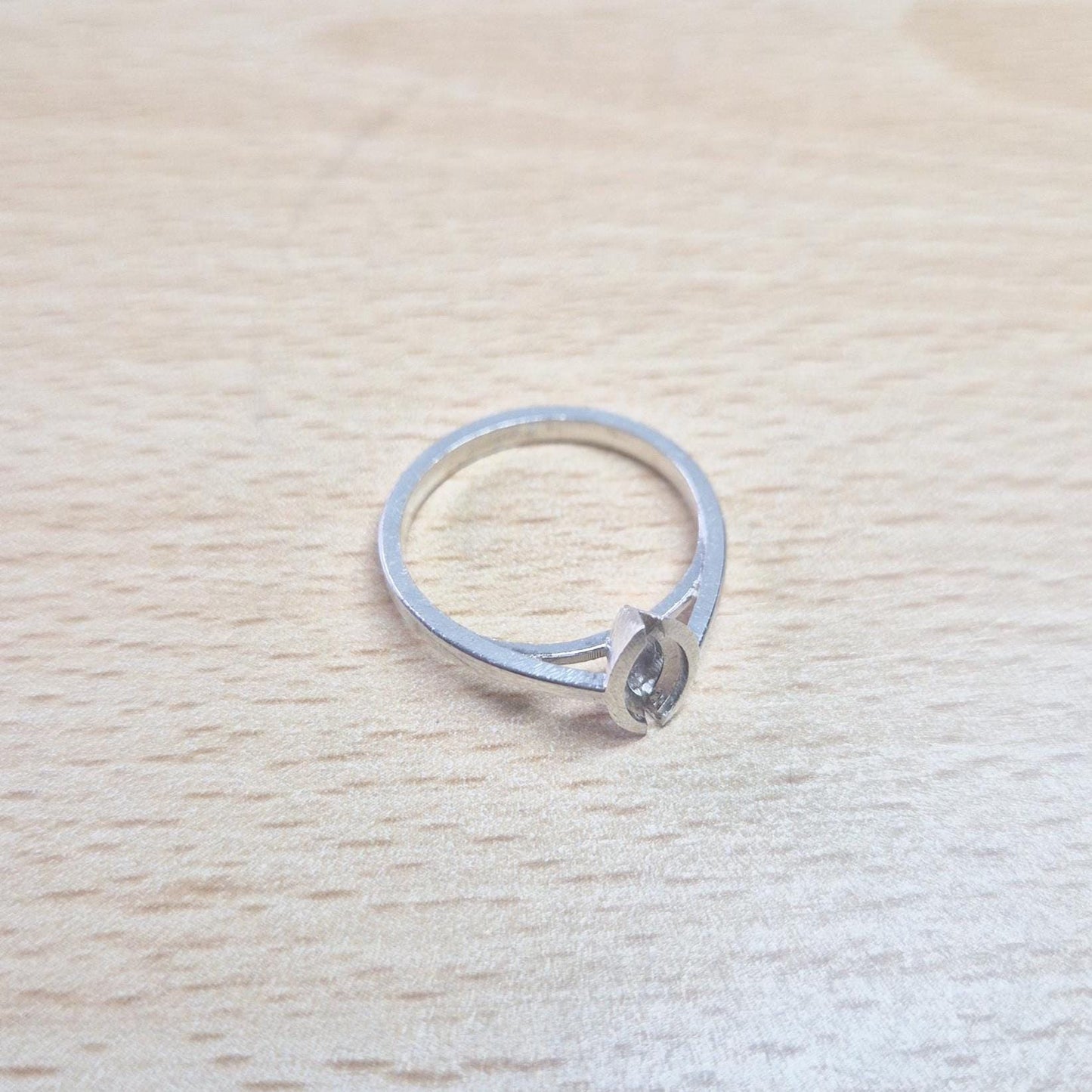 Silver marquise split bezel ring blank lying flat on a light wooden surface, viewed from above, showing the empty marquise-shaped split bezel and the entire ring.