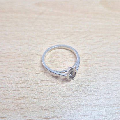 Silver marquise split bezel ring blank lying flat on a light wooden surface, viewed from above, showing the empty marquise-shaped split bezel and the entire ring.