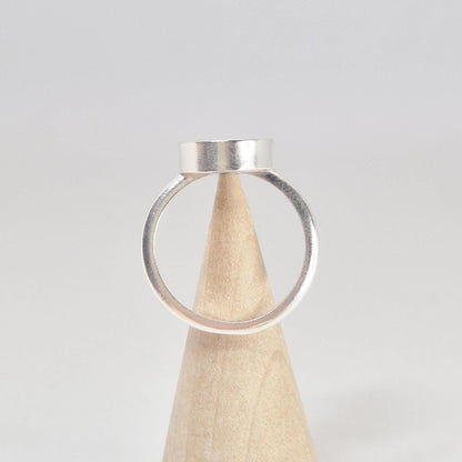 Rear view of an empty sterling silver oval cabochon ring setting, displayed on a light wood conical stand.