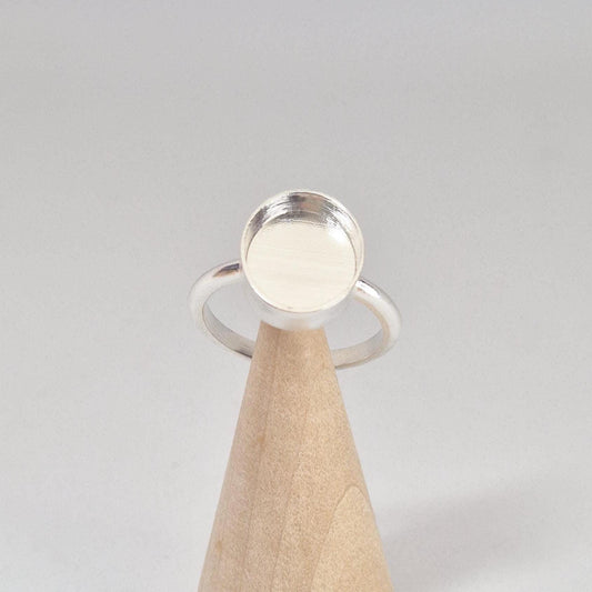 Front-angled view of an empty sterling silver oval cabochon ring setting, displayed prominently on a light wood conical stand.