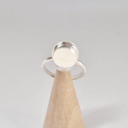 Front-angled view of an empty sterling silver oval cabochon ring setting, displayed prominently on a light wood conical stand.