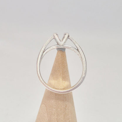 Back view of a split shank silver ring with an elevated V-prong setting, presented on a wooden cone.