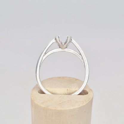 Front view of a silver split shank ring setting on a cylindrical wooden stand, highlighting the V-prong mount.