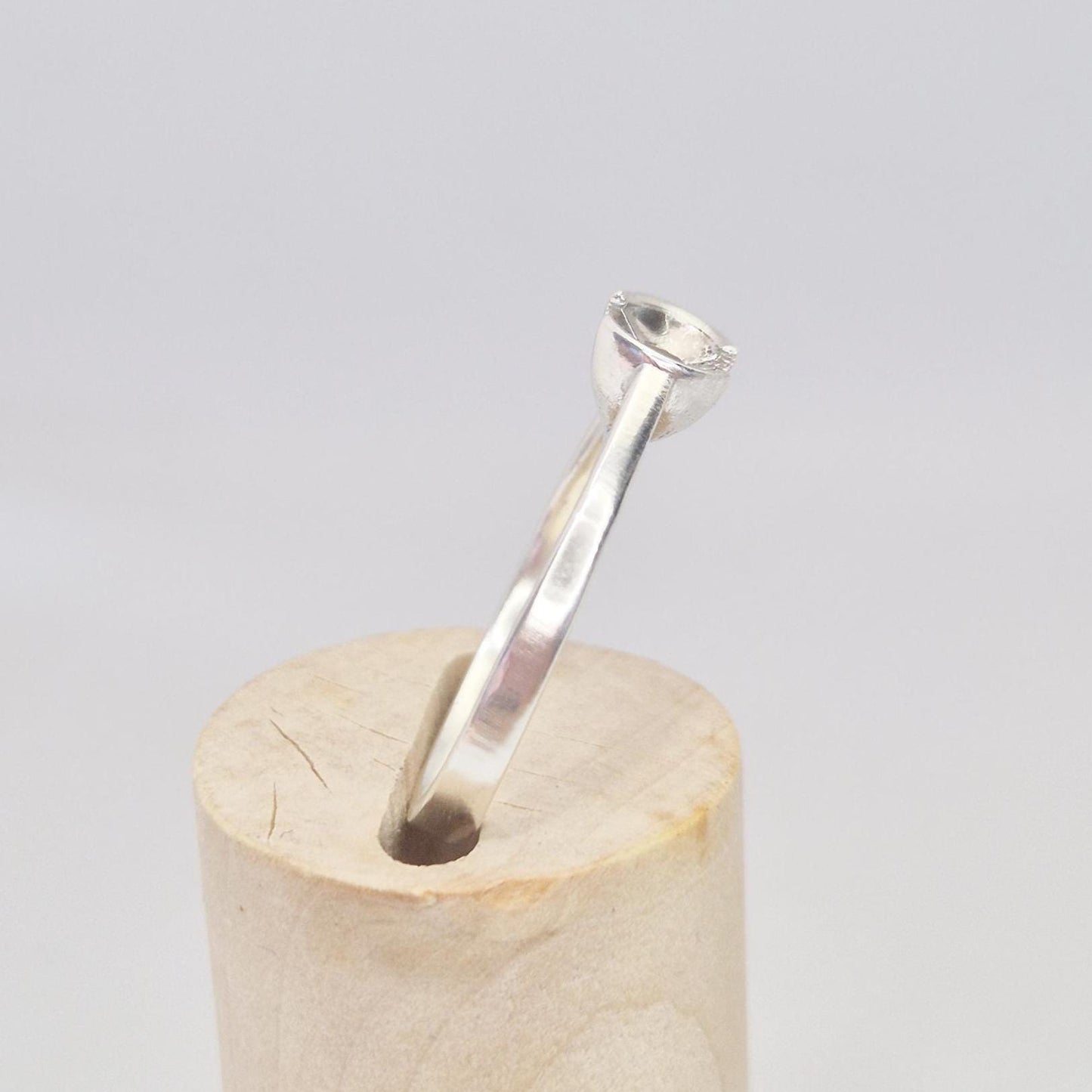 Side profile of the silver solitaire ring on a wooden cylinder, showing the band curvature and mounting cup.