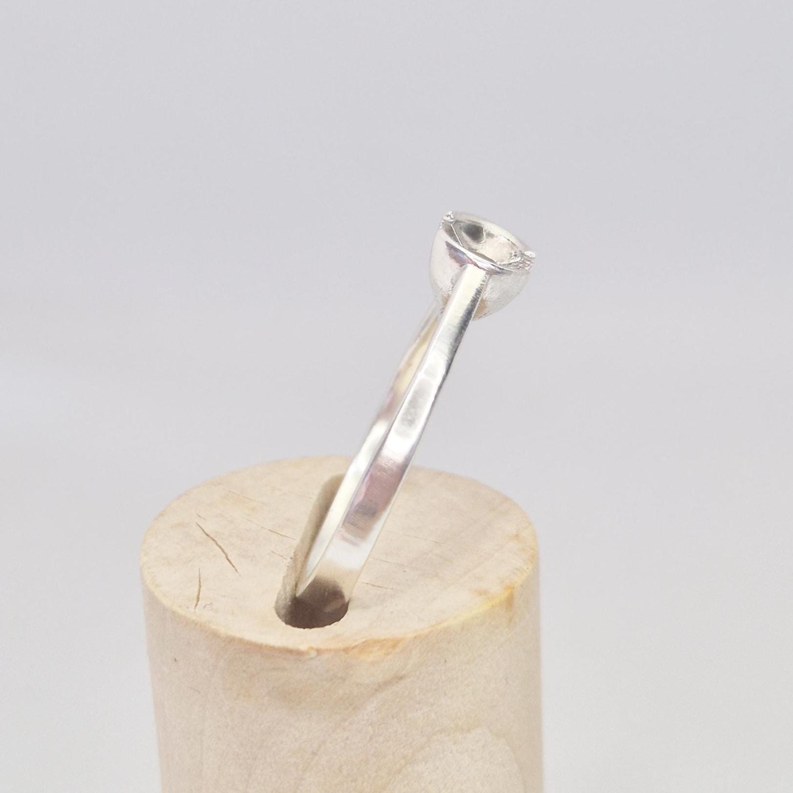 Side profile of the silver solitaire ring on a wooden cylinder, showing the band curvature and mounting cup.