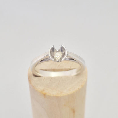 Angled front view of a silver ring with an open cup setting, ideal for custom gemstone setting, shown on a wooden base.