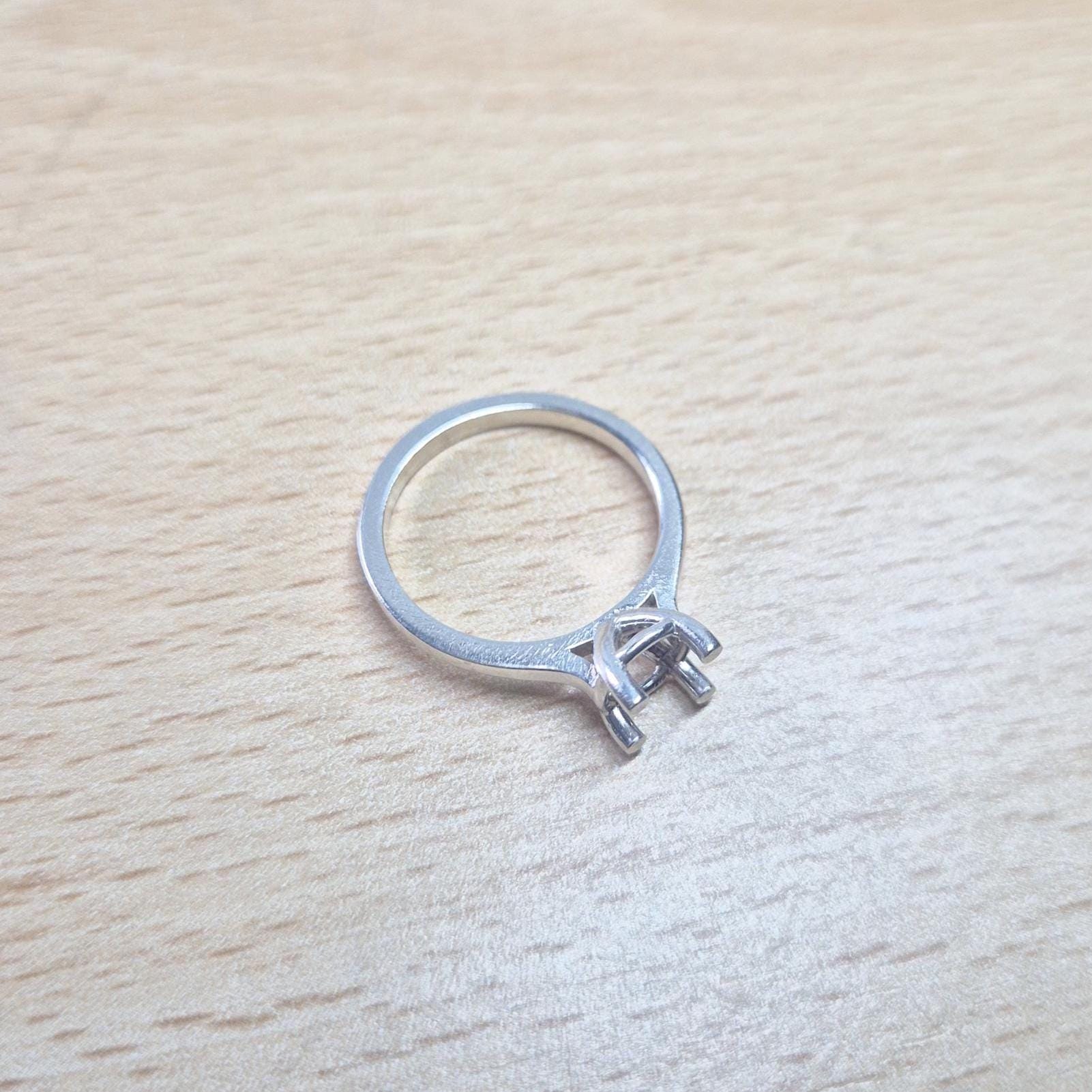 Sterling silver ring setting with a four-prong square head, resting on a light wood surface, providing a clear, slightly elevated view of the entire ring.