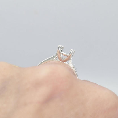 Close-up view of a sterling silver ring setting with a four-prong square head, shown on a finger from a slightly elevated angle, emphasizing the open basket-style setting beneath the prongs.