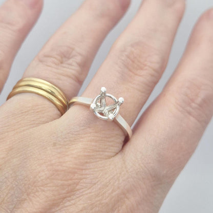 Sterling silver ring setting with a four-prong square head, worn on a hand with another plain gold band. The ring is oriented with the prongs facing up.
