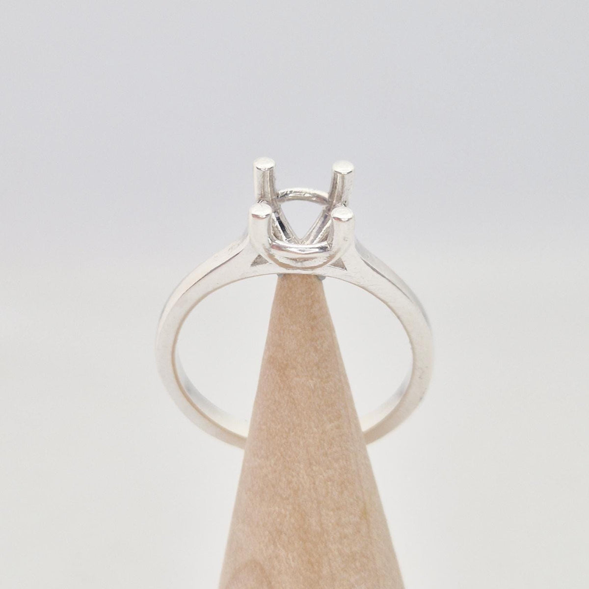 Sterling silver ring setting with a four-prong square head, displayed on a conical wooden stand. The band is smooth and polished.