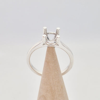 Sterling silver ring setting with a four-prong square head, displayed on a conical wooden stand. The band is smooth and polished.