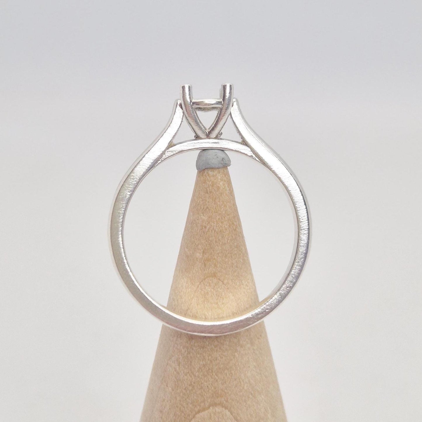 Back view of a sterling silver ring setting with a four-prong round head, displayed on a conical wooden stand, illustrating the full circular band and the base of the setting.