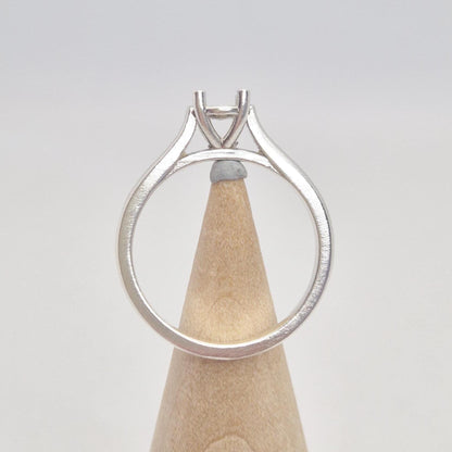 Back view of a sterling silver ring setting with a four-prong round head, displayed on a conical wooden stand, illustrating the full circular band and the base of the setting.