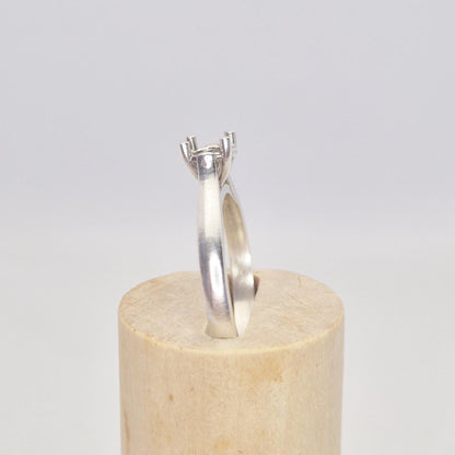 Side view of a sterling silver ring setting with a four-prong round head, angled on a conical wooden stand, showcasing the tapered band leading up to the setting.