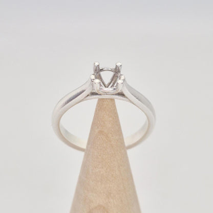 Front view of a sterling silver ring setting with a four-prong round head, positioned centrally on a conical wooden stand, emphasizing the classic, simple design.