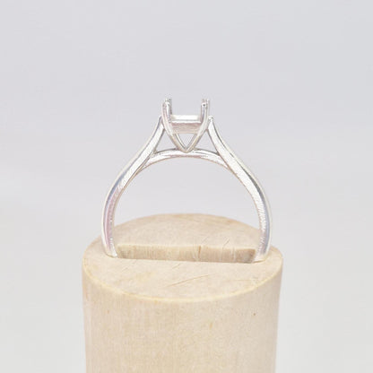 Side view of a silver ring setting with a four-prong princess cut head, angled on a conical wooden stand, emphasizing the smooth, tapered band leading to the setting.