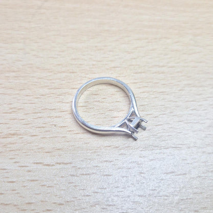 Sterling silver ring setting with a four-prong princess cut head, resting on a light wood surface, providing an overhead view of the full ring and its open setting.