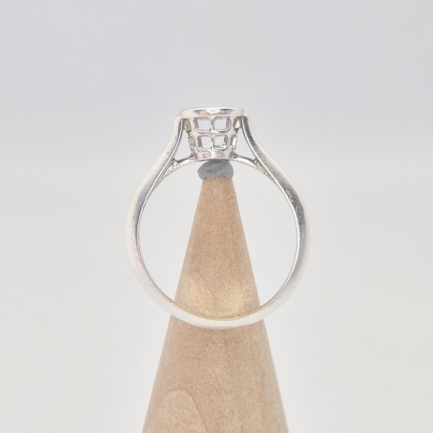 Side view of a silver ring setting with an empty round bezel, displayed upright on a light wooden cone. The ring band is smooth and tapers slightly towards the setting.