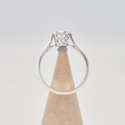 Side view of a silver ring setting with an empty round bezel, displayed upright on a light wooden cone. The ring band is smooth and tapers slightly towards the setting.