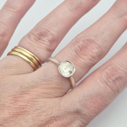 Sterling silver ring setting with a cushion cut bezel, worn on a hand with an additional plain gold band, showcasing the ring's appearance on a finger.