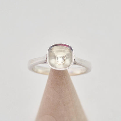 Front view of a sterling silver ring setting with a cushion cut bezel, displayed on a conical wooden stand, emphasizing the rounded square shape of the bezel.