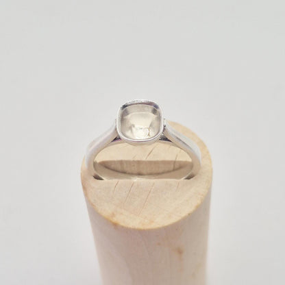 Top-down view of a sterling silver ring setting with a cushion cut bezel, positioned on a short, wide conical wooden stand, highlighting the soft square shape of the bezel.