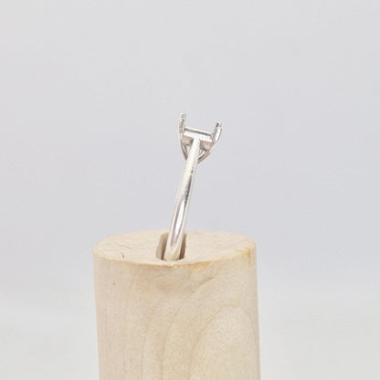 Silver cathedral setting princess cut ring blank inserted into a cylindrical wooden ring holder, viewed from the side, highlighting the raised empty four-prong setting.