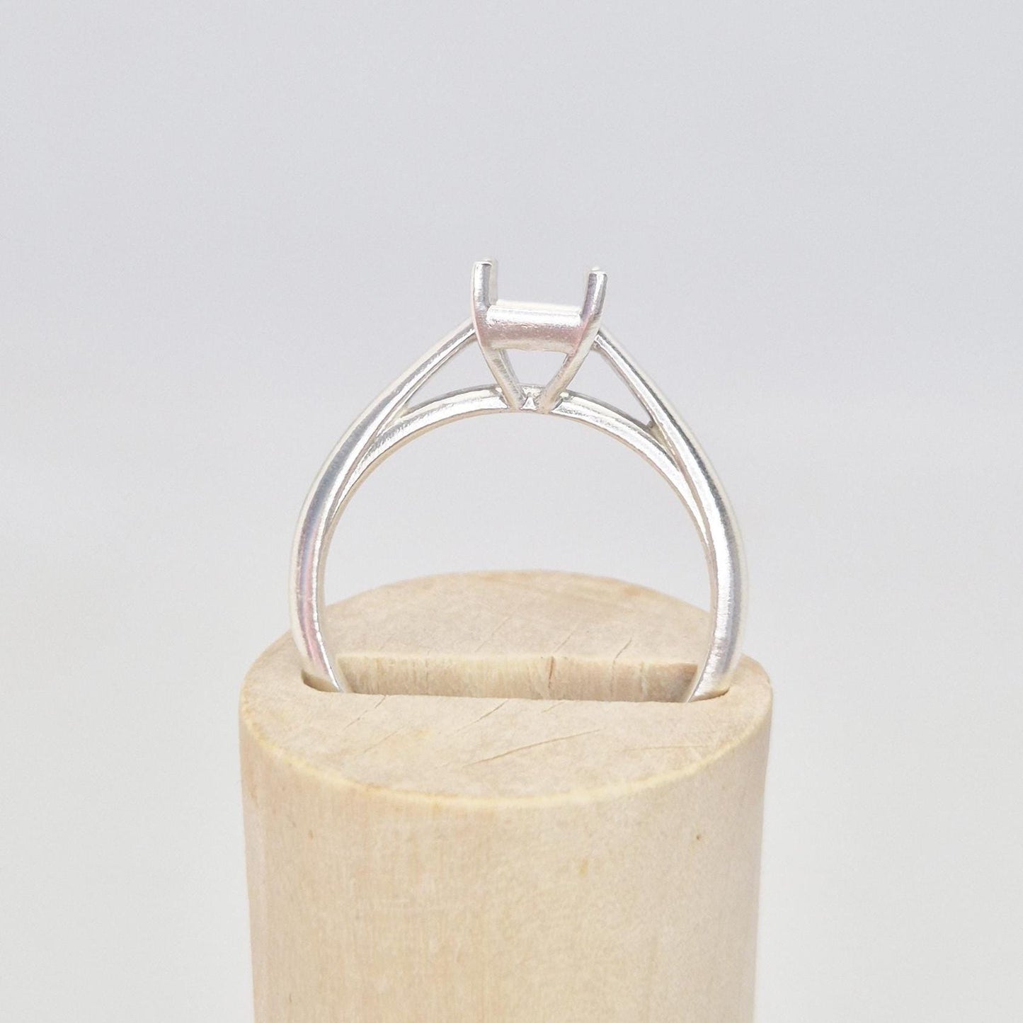 Silver cathedral setting princess cut ring blank resting on a cylindrical wooden ring holder, viewed from the front, showing the empty four-prong setting and the top of the band.