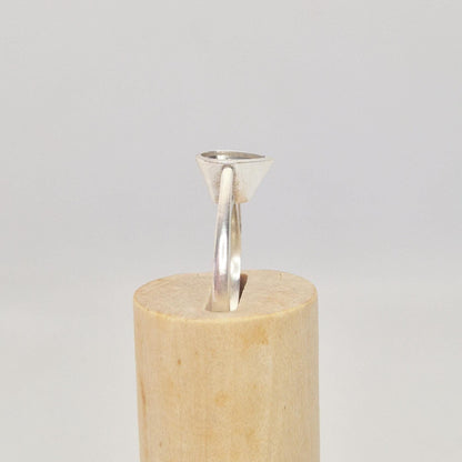 Side profile of a silver pear cut bezel cathedral ring blank partially inserted into a cylindrical wooden ring holder, showing the angle of the pear-shaped bezel.