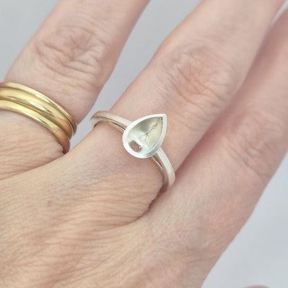Silver pear cut bezel cathedral ring blank on a hand, next to a plain gold band, showing how the pear-shaped setting sits on a finger.
