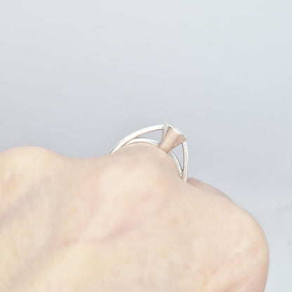 Close-up of a silver pear cut bezel cathedral ring blank on a hand, focusing on the empty pear-shaped bezel and the ring's design when worn.