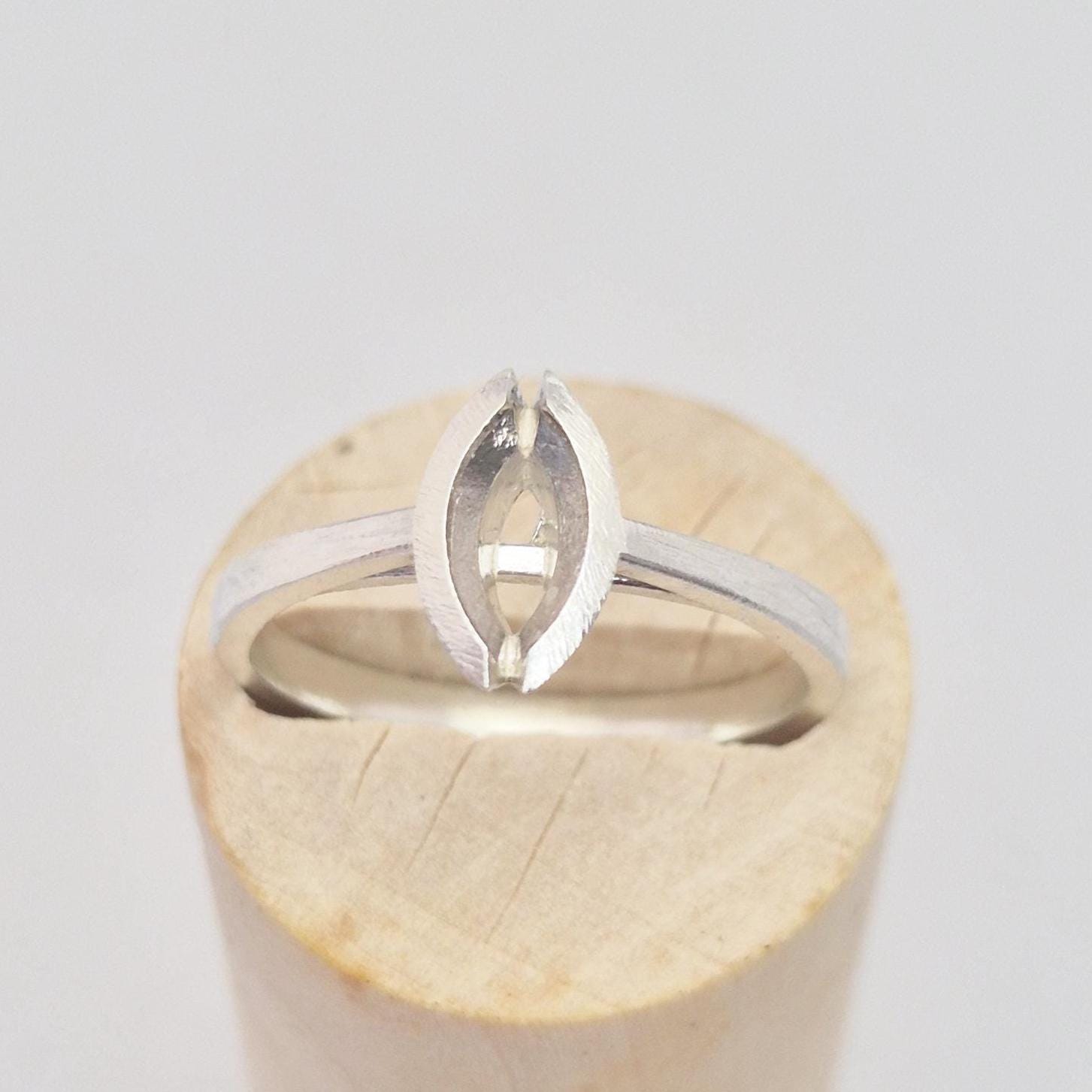 Silver marquise split bezel ring blank inserted into a cylindrical wooden ring holder, front view, highlighting the empty marquise-shaped split bezel setting.