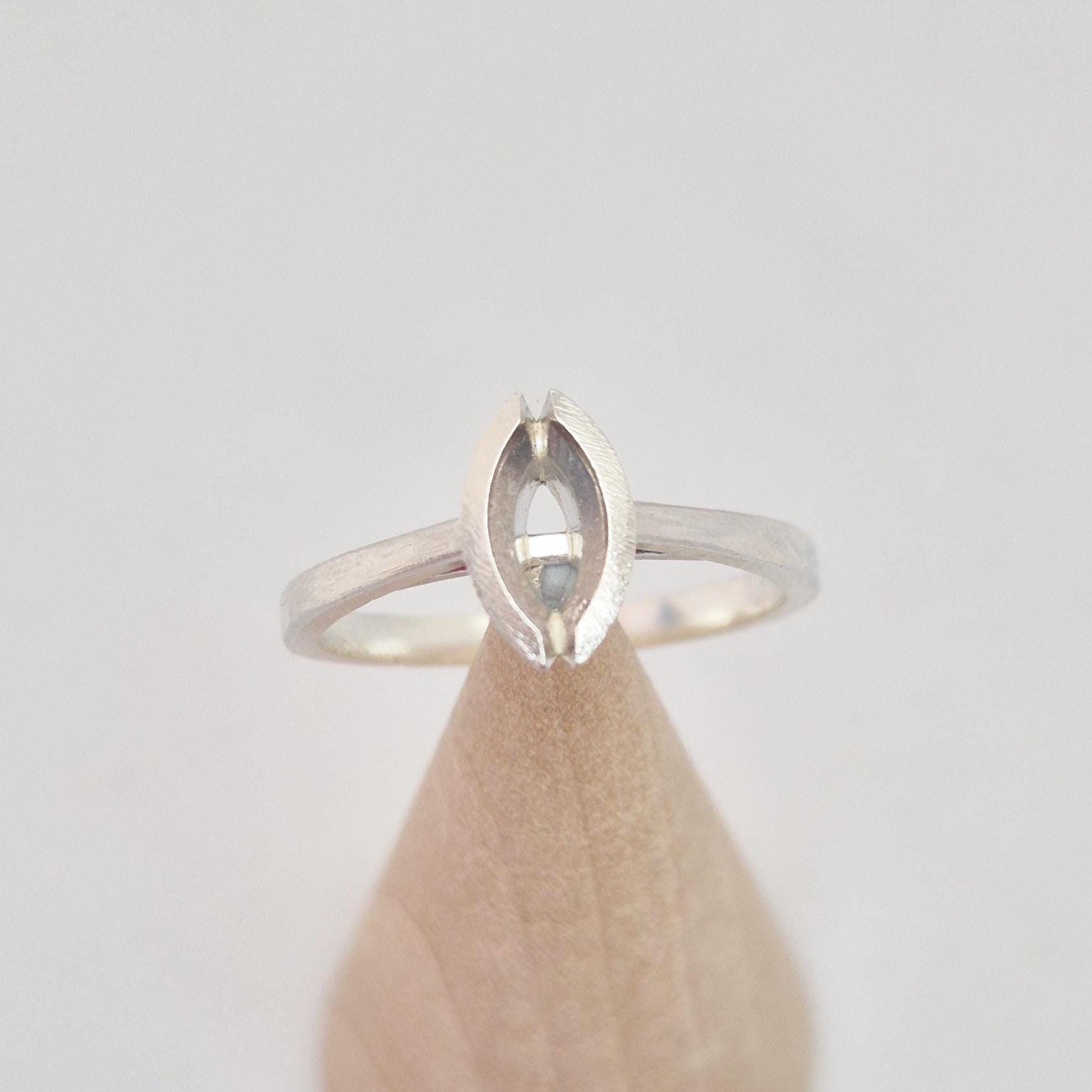 Silver marquise split bezel ring blank inserted into a conical wooden ring holder, top-down view, clearly showing the empty marquise-shaped split bezel.