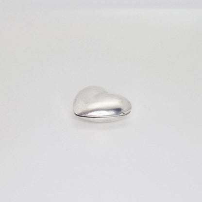 A closed, puffed silver heart locket seen from the back, showing the seam where the two halves join and its rounded contours on a plain white background.
