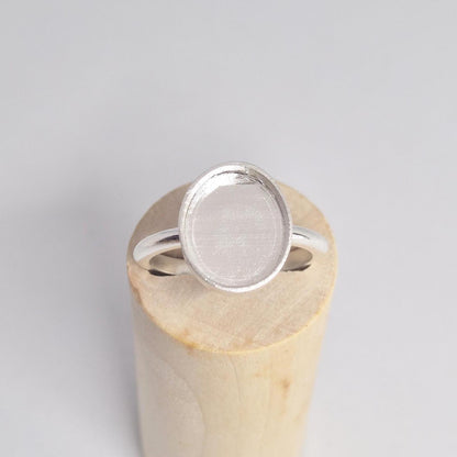 Overhead view of an empty sterling silver oval cabochon ring setting, with the band resting horizontally on a light wood cylindrical display.
