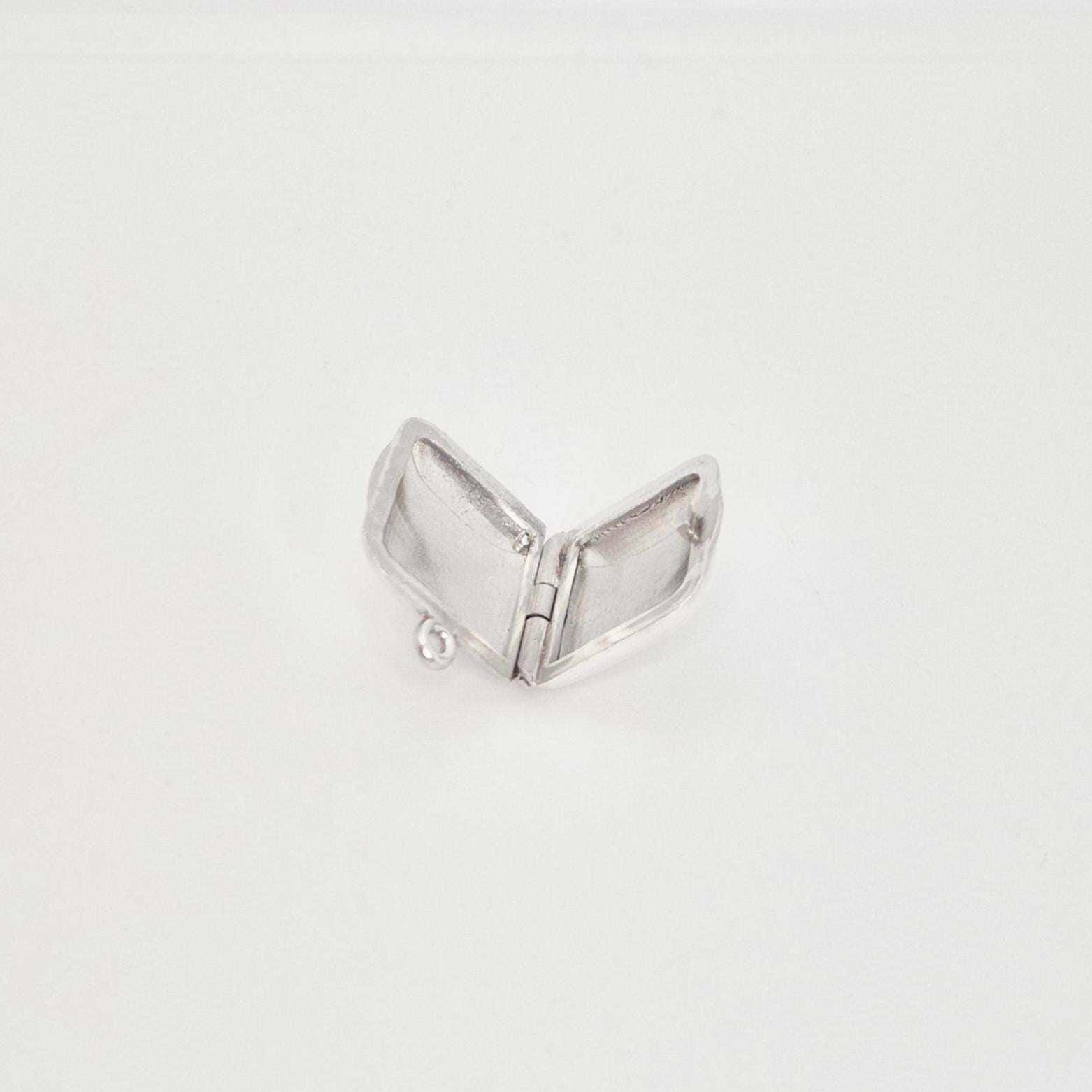 A blank sterling silver square locket pendant opened flat, revealing the two internal compartments and the small ring at the top for attachment, set against a plain white background.