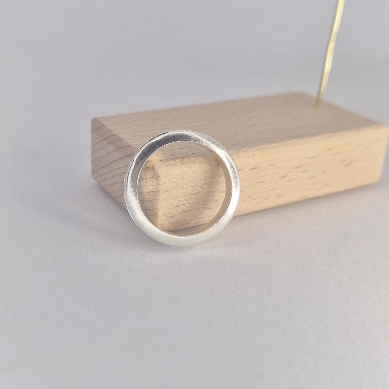 Slim silver channel ring with softly curved profile, photographed upright against a pale wooden display block on a clean white background.